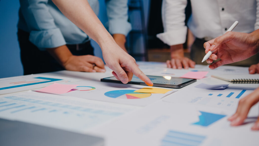 Empresários e empresárias, reunidos para debater ideias sobre novos colegas de projetos de papelada, trabalhando juntos, planejando uma estratégia de sucesso, desfrutam do trabalho em equipe em um pequeno escritório noturno moderno.