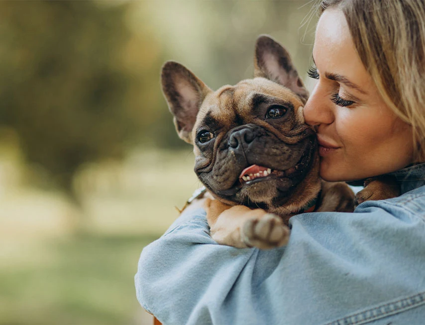 Imagem composta por uma mulher, abraçando e beijando o seu cachorro que está no colo, a imagem retrata aborda sobre as cidades pet friendly