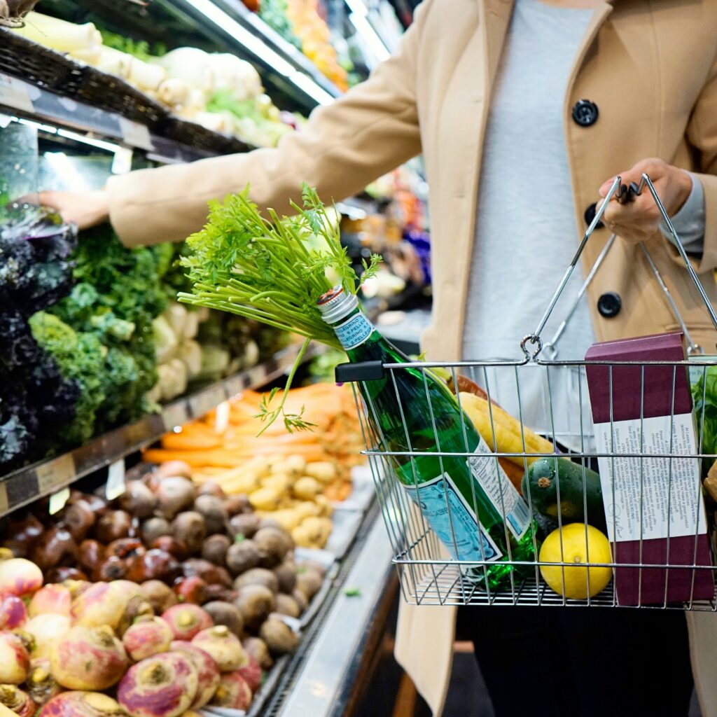 Mulher fazendo compras no mercado, carregando uma cesta com diversos produtos.