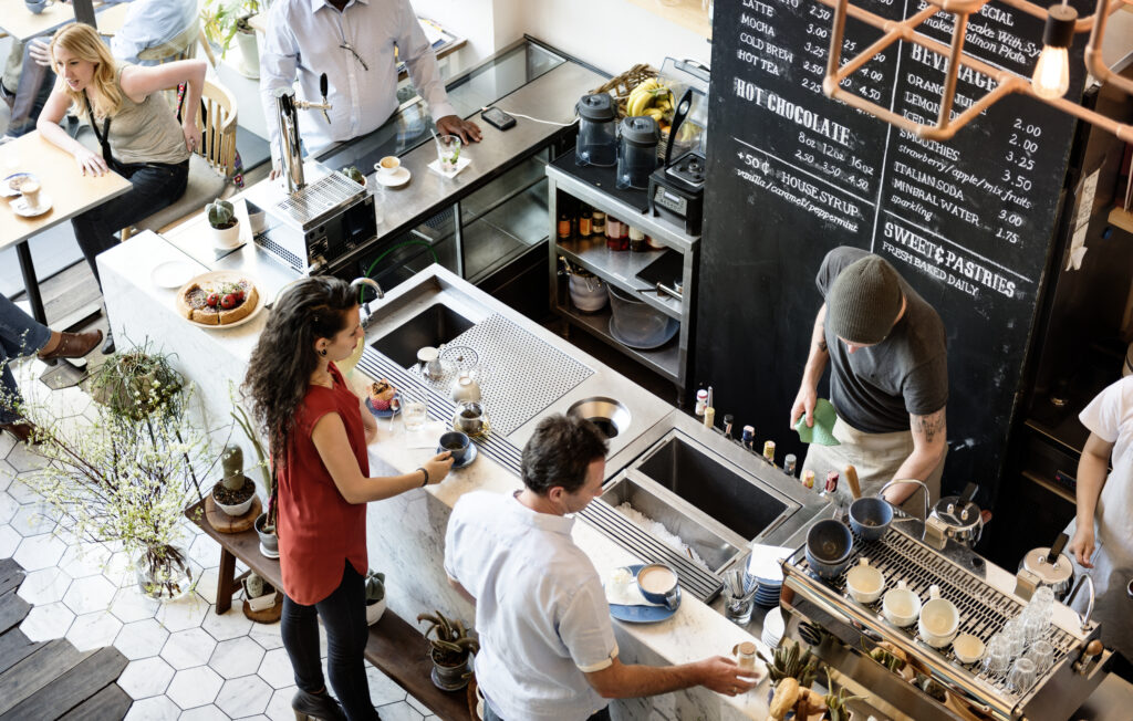 Clientes aproveitando o ambiente de uma cafeteria, enquanto atendentes trabalham no balcão.