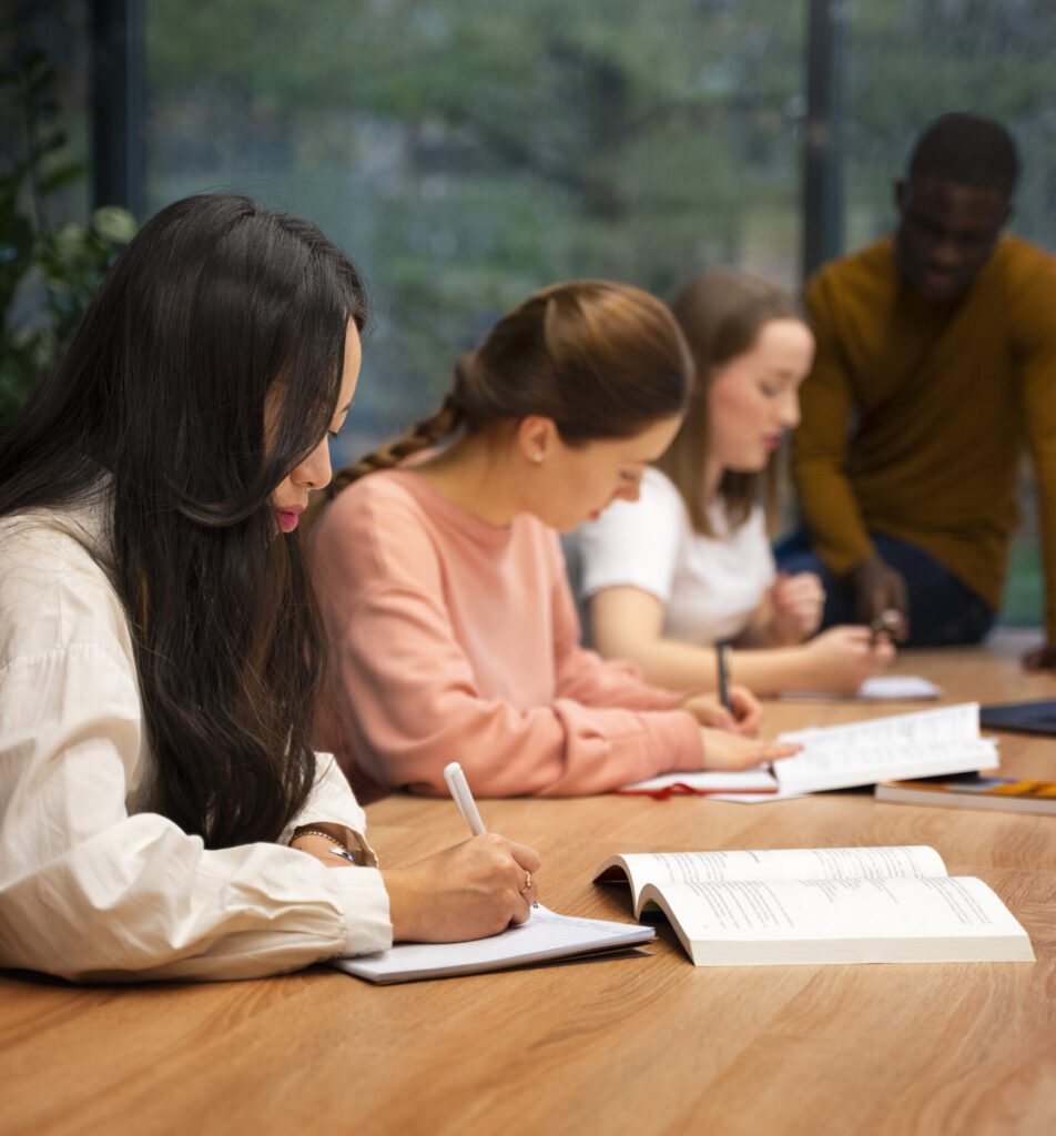 Grupo de universitários reunido em uma mesa de biblioteca, estudando e trocando ideias.